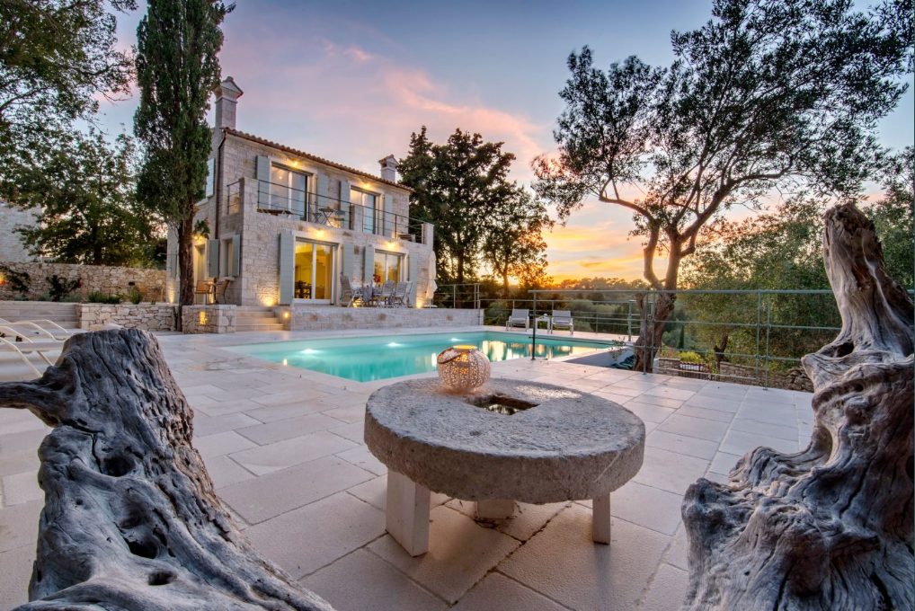 Perla House at dusk, the pool lit and the sky turning pink behind the olive trees